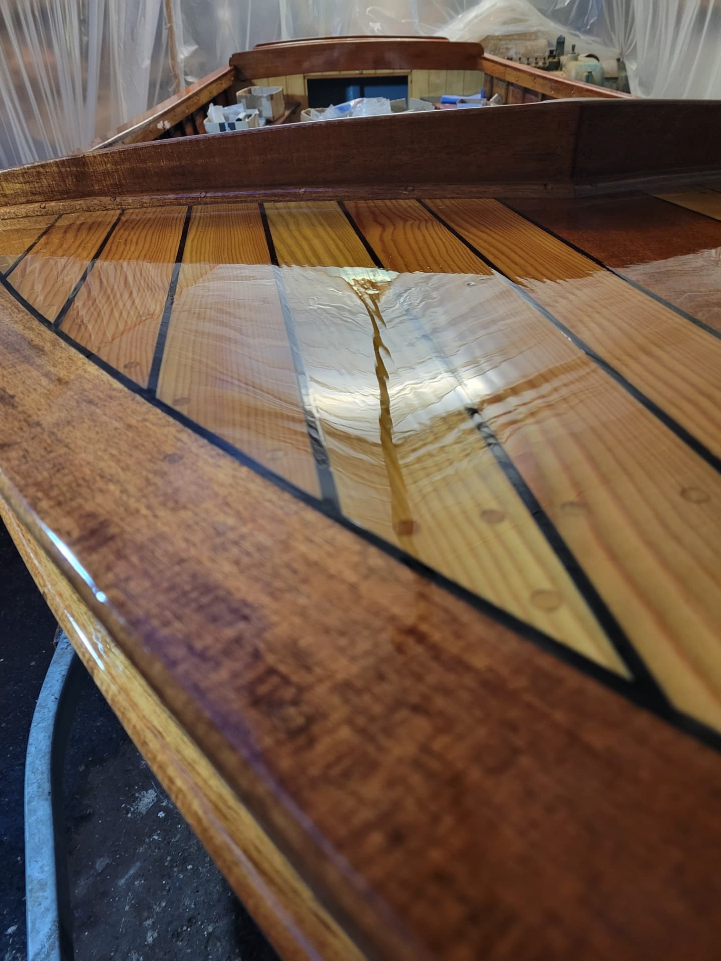 Freshly varnished wooden boat deck reflecting the workshop lights